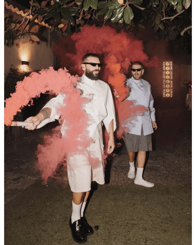 Two newlyweds walking through a cloud of pink smoke during the party